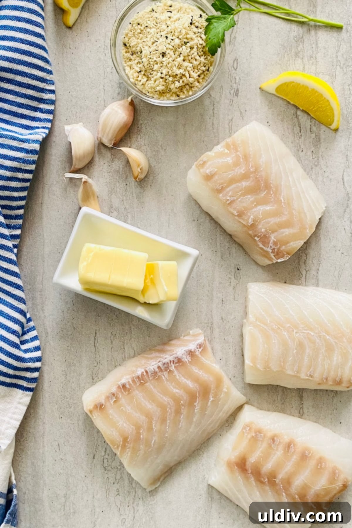 Golden-Crisp Garlic Herb Panko Baked Cod 4 A vibrant flat lay showcasing the fresh ingredients for baked cod: raw cod fillets, a lemon, a stick of butter, fresh garlic cloves, and parsley.