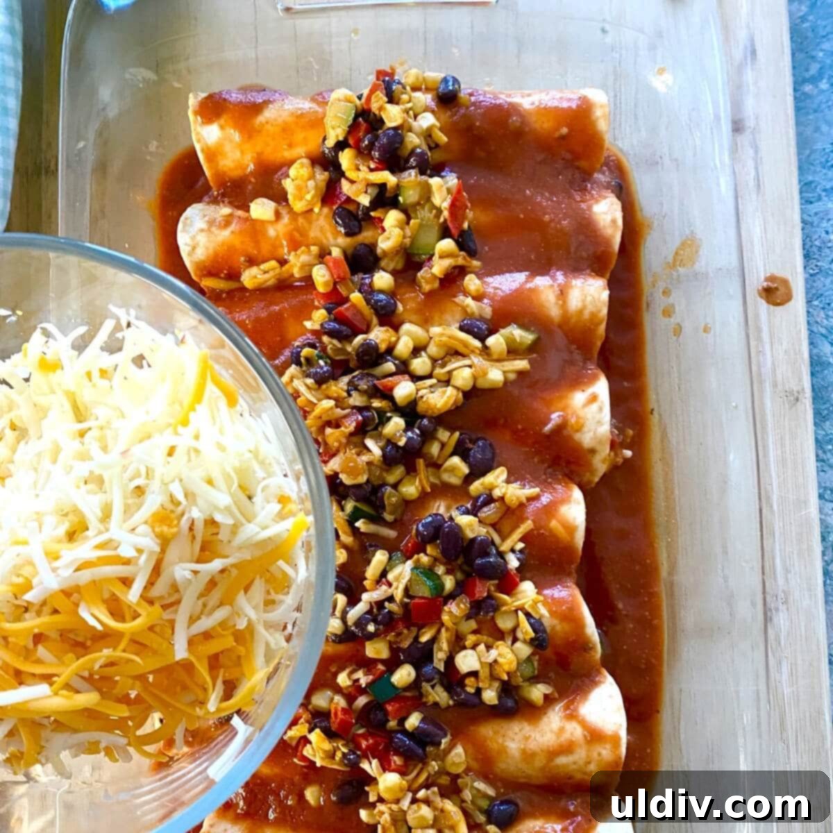 Effortless Healthy Black Bean Enchiladas 9 A close-up of unbaked enchiladas in a pan, fully covered with sauce, and a generous layer of shredded cheese sprinkled on top, ready for the oven.