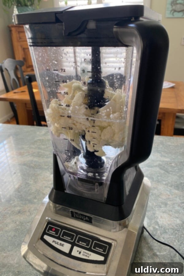 Easy 20-Minute Cauliflower Pilaf 4 Close-up shot of a blender with cauliflower florets and water, illustrating the process of easily making cauliflower rice at home.