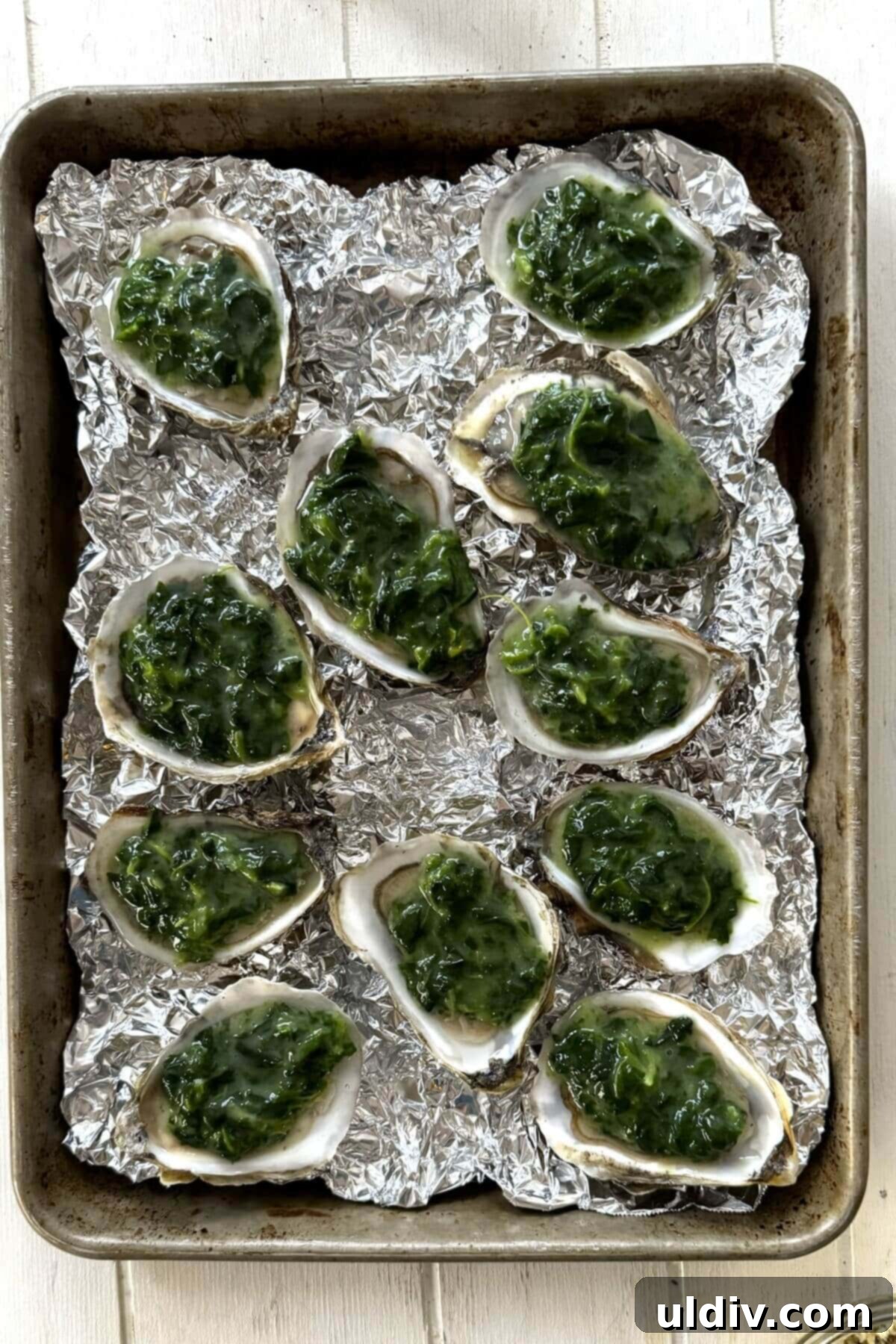 Indulgent Oysters Rockefeller 8 Shucked oysters topped with creamed spinach on a baking sheet.