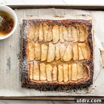 apple tart on a baking sheet with apricot jam in a bowl.