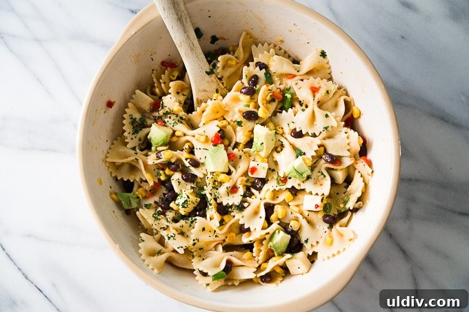 Southwest Pasta Salad embraces the sweetness of cream style corn, along with the spiciness of chipotle sauce that is perfect to serve on a hot summer day! Southwest Pasta Salad with wooden spoon.