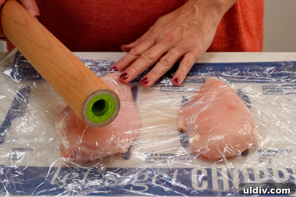 Juicy Oven-Baked Chicken Breasts with Garlic and Herbs 3 A woman pounding a chicken breasts with a rolling pin.